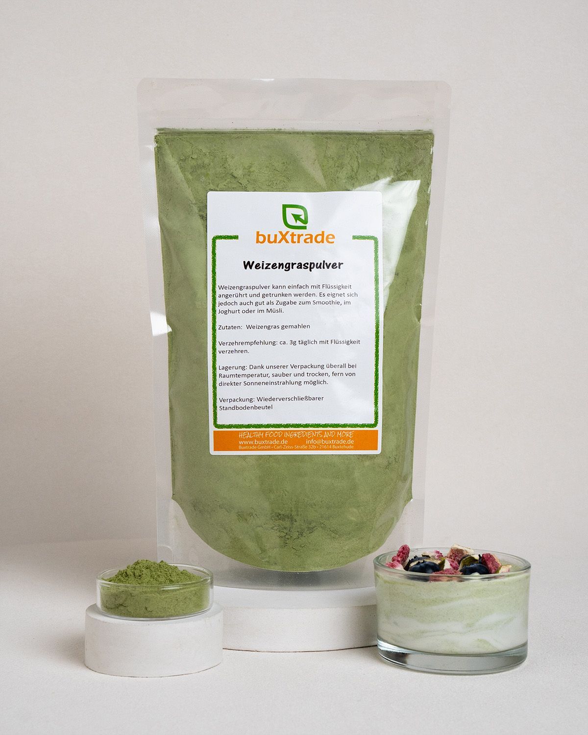 Verpackung mit grünem Pulver, daneben Schale mit Pulver und Glas mit Inhalt. Etikett mit Produktname 'buXtrade'.