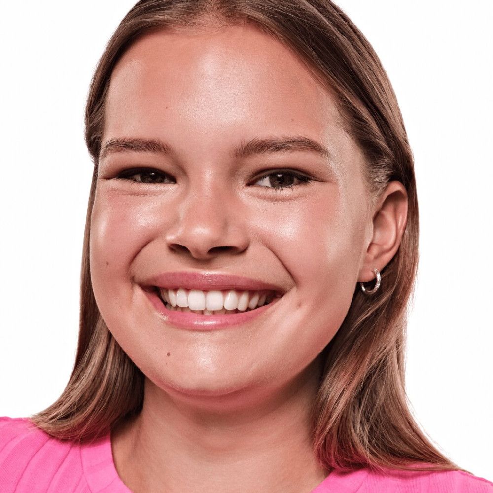 Porträt einer lächelnden jungen Frau. Sie trägt ein rosa Oberteil. Ihr Haar ist braun und schulterlang.