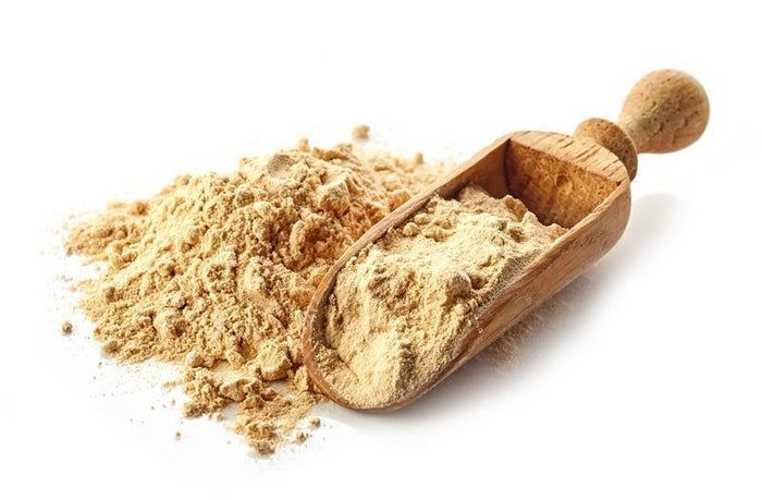 Haufen und Löffel von buXtrade Bio Maca Pulver. Holzschaufel mit Pulver. Haufen Pulver daneben.