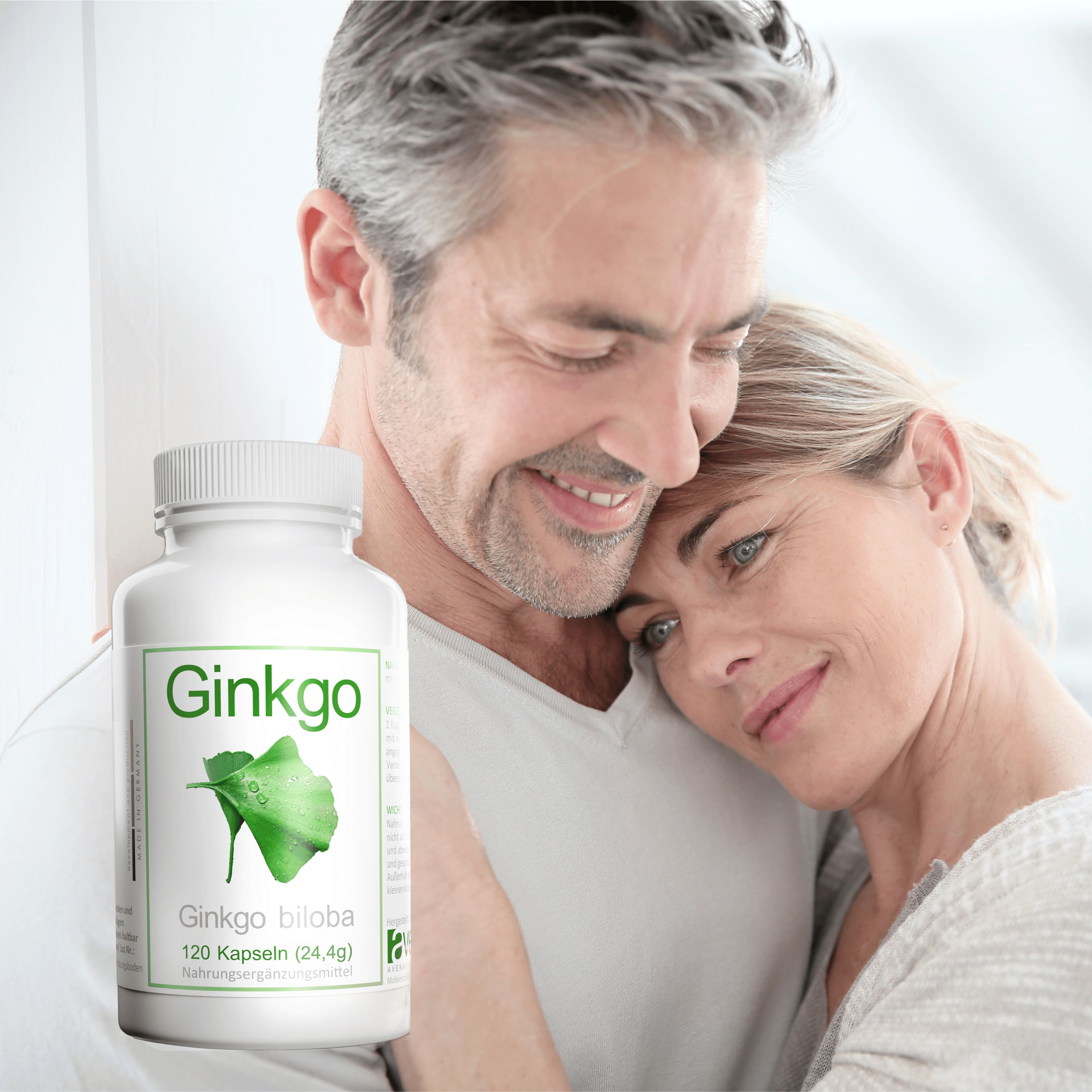 Paar umarmt sich, im Vordergrund Flasche mit Ginkgo-Kapseln. Etikett mit Blattmotiv und Produktinformationen.