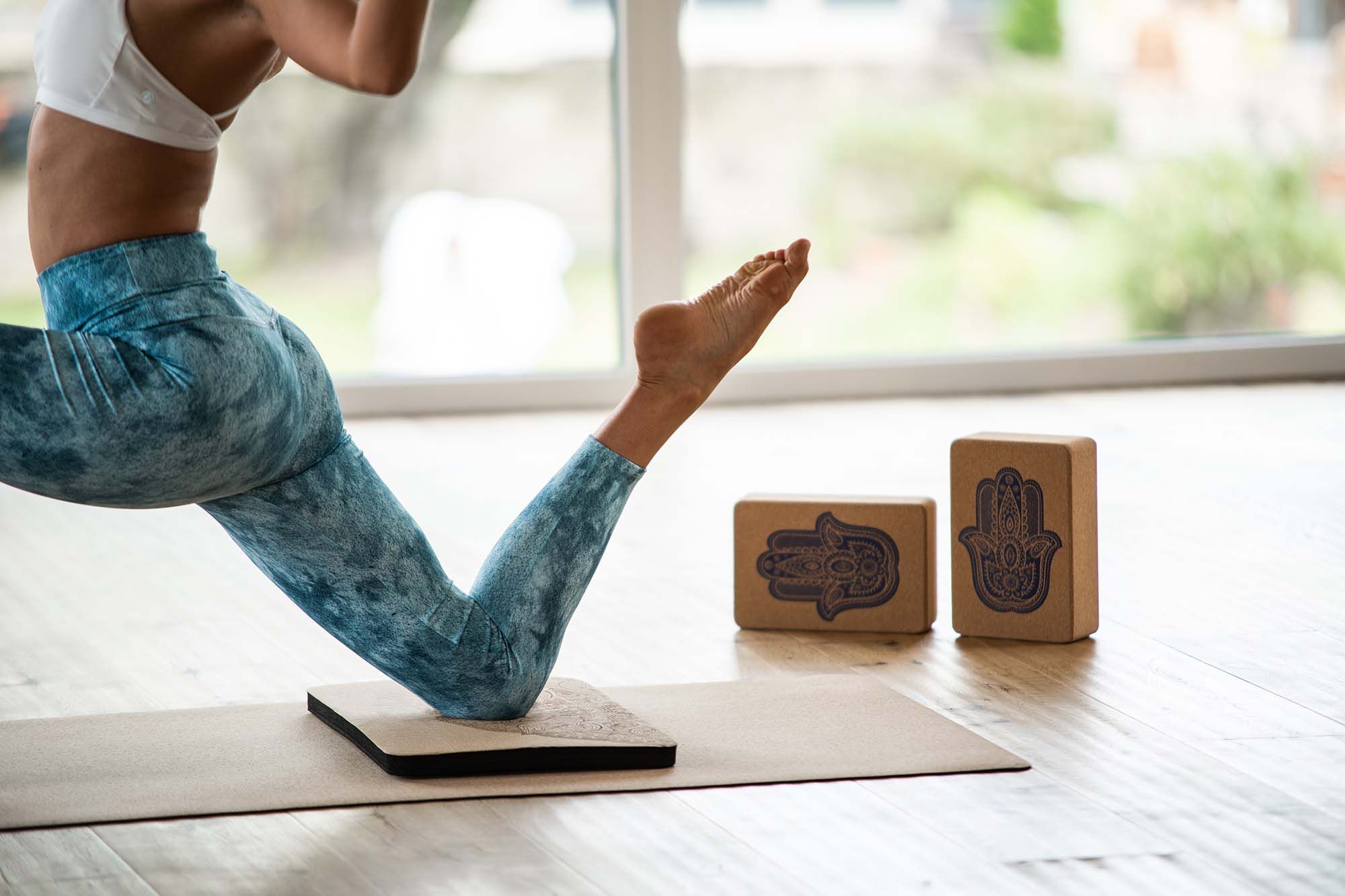 Person in Yoga-Pose. Kniekissen und Yoga-Blöcke mit Hand-Symbol. Yoga-Matte.