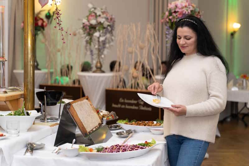 Frau nimmt Honigwabe von einem Buffet. Im Hintergrund weitere Speisen und Dekorationen.