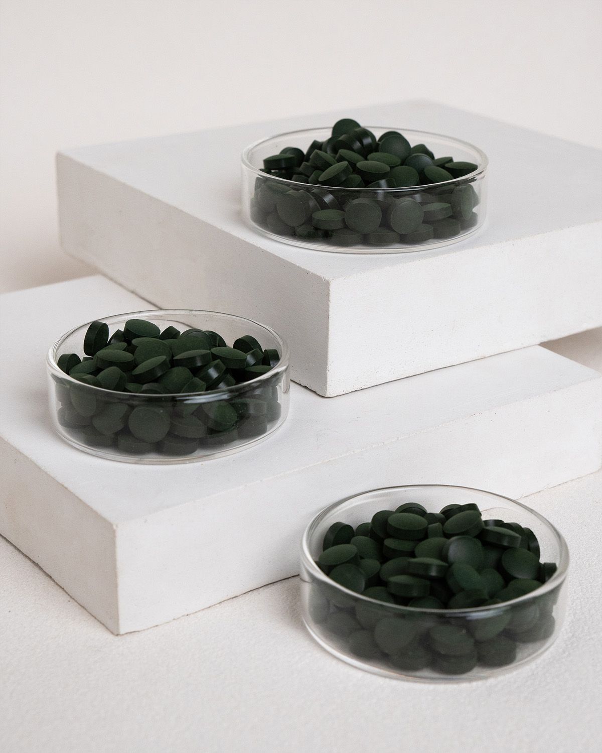 Drei Schalen mit grünen Tabletten auf weißen Blöcken. Die Tabletten sind rund und dunkelgrün.
