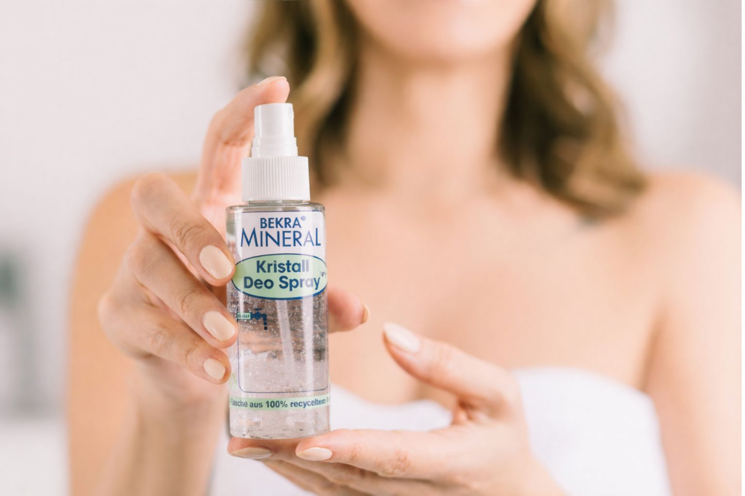 Nahaufnahme einer Flasche BEKRA Mineral Kristall Deo Spray, gehalten von Händen. Transparente Flasche mit Kristallen.