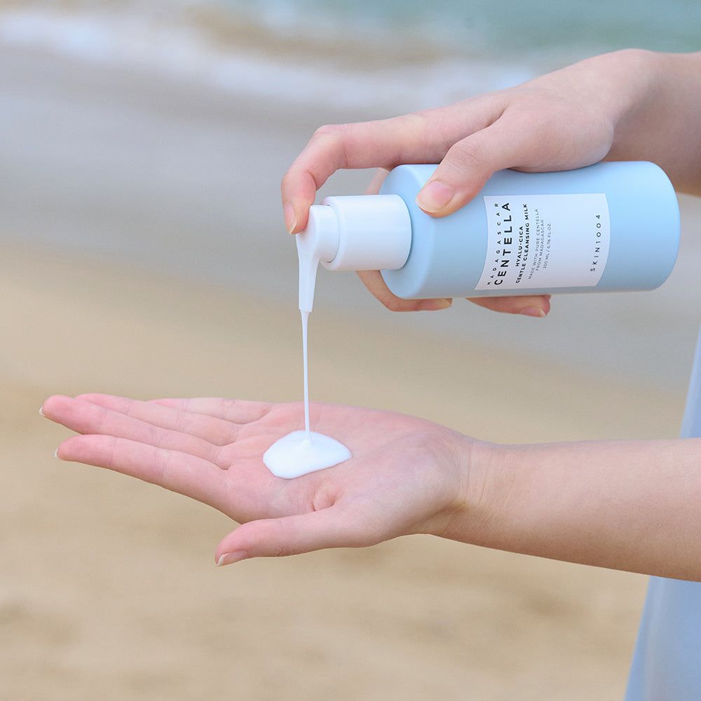 Hände halten hellblaues Fläschchen mit weißem Pumpkopf. Produkt wird in die Handfläche gegossen. Aufkleber mit Text: SKIN1004.