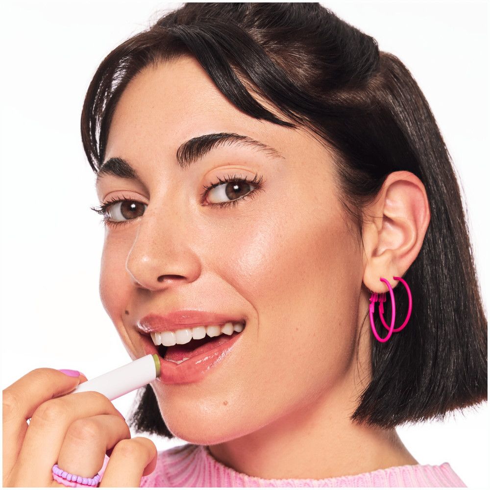 Frau mit Lippenbalsam. Weißer Stift mit grünem Balsam. Aufschrift Juicy Bomb und Essence.