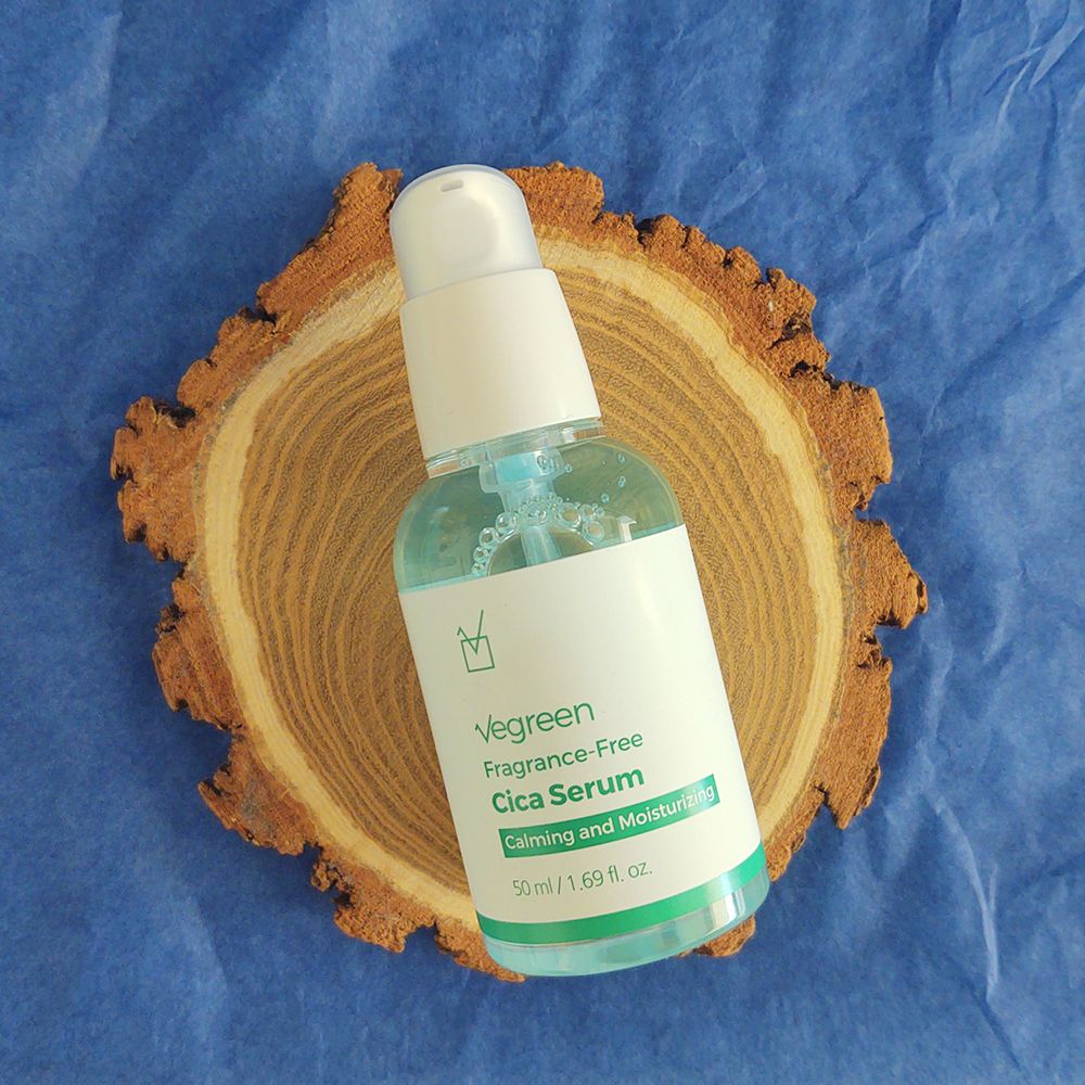 Gesichtsserum-Flasche auf Holzscheibe. Weißer Pumpdeckel, grüne und weiße Etiketten mit Text. Blaue Flüssigkeit sichtbar.