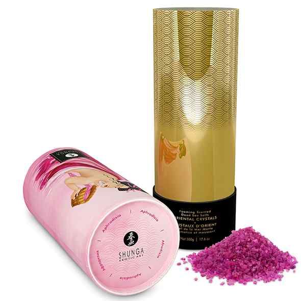 Zylindrischer Behälter, rosa, mit Frau und Produktnamen. Daneben ein Haufen pinkfarbener Kristalle.