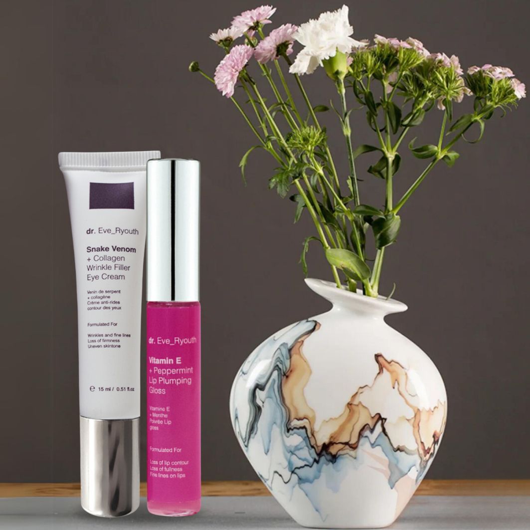 Dr. Eve_Ryouth Augencreme und Lippenpflege neben einer Vase mit Blumen.