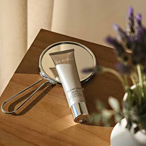 Silberfarbene Tube auf Tisch mit Spiegel und Blumen. Produktname und Schriftzug.