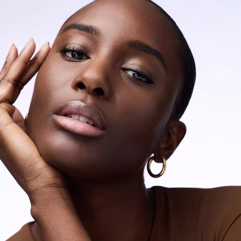 Porträt einer Frau mit dunkler Haut und dunklen Haaren. Sie trägt goldene Ohrringe.