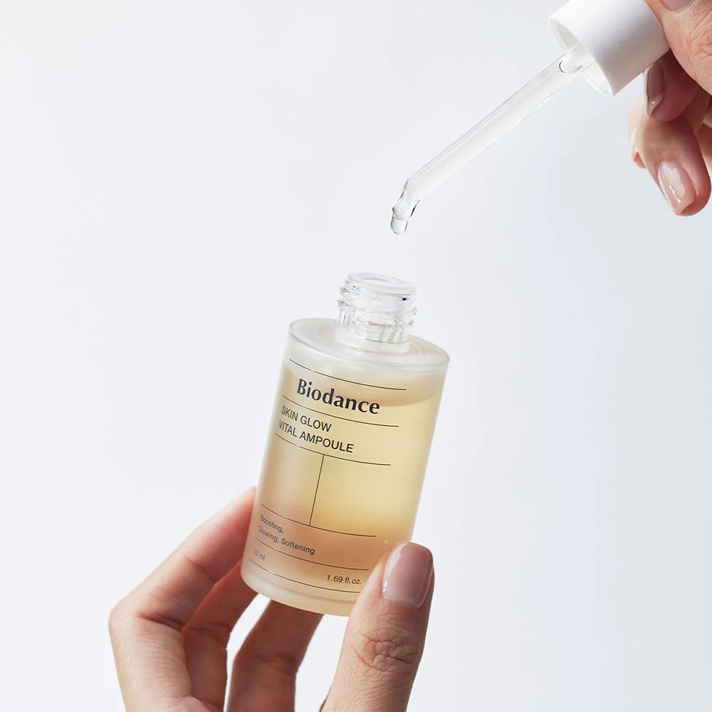 Hände halten Serumflasche mit Pipette. Tropfen fallen aus der Pipette. Aufschrift: Biodance Skin Glow Vital Ampoule.