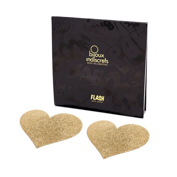 Zwei goldfarbene, herzförmige Nippelcover mit Glitzer neben einer schwarzen Verpackung. Aufdruck: Bijoux Indiscrets.