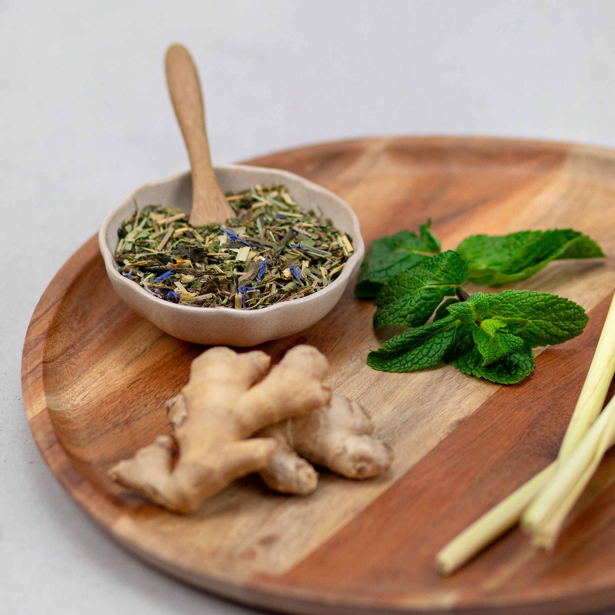 Holztablett mit Kräutern, Ingwer, Minze und Zitronengras. Schale mit Kräutern und Holzlöffel.