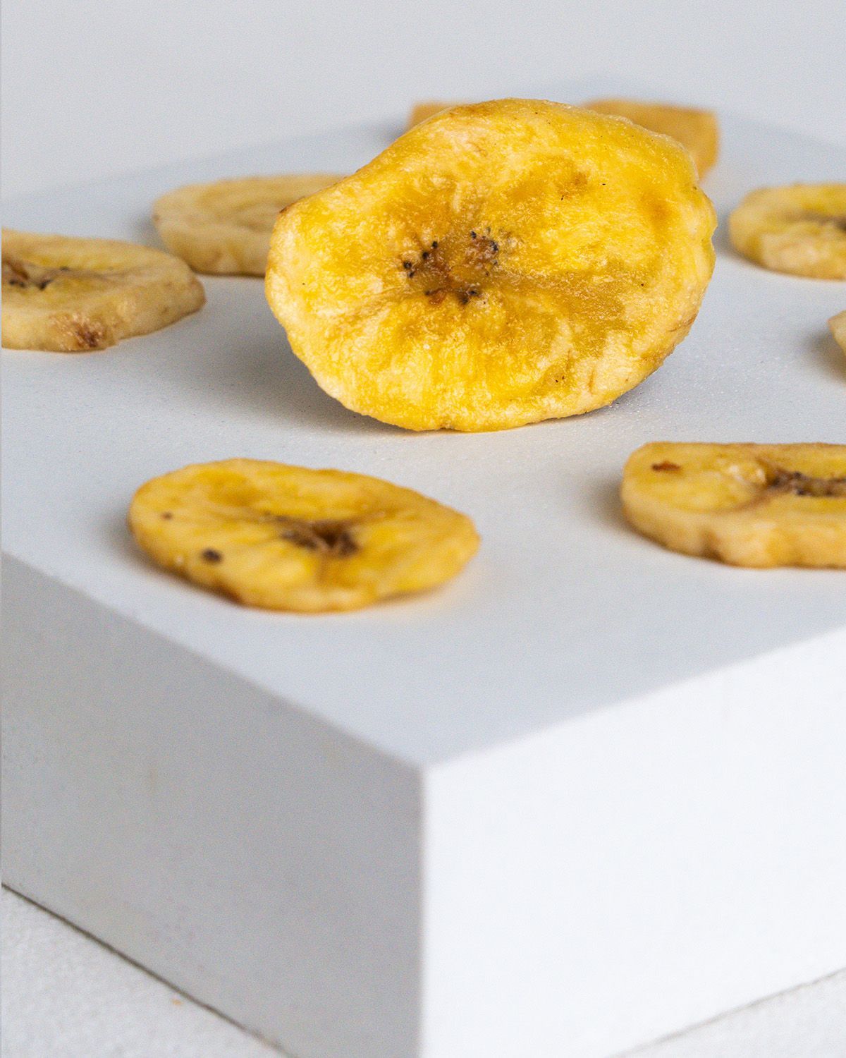 Nahaufnahme von Bio Bananenchips auf einer weißen Oberfläche. Einzelne Chips sind sichtbar.