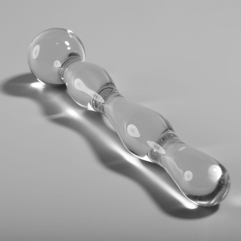 Dildo aus Borosilikatglas. Klar, mit abgerundeten Formen. Besteht aus Kugel, zwei Wölbungen und einem länglichen Ende. Liegt auf hellem Untergrund.