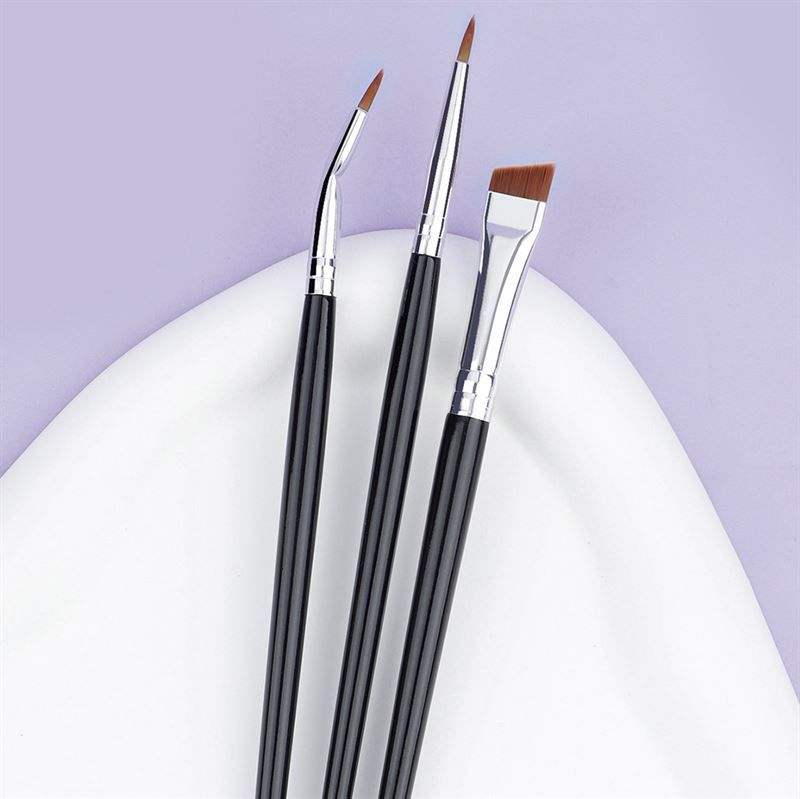 Drei Make-up-Pinsel auf weißer, geschwungener Oberfläche. Schwarze Griffe, silberne Metallhülsen. Verschiedene Pinselköpfe.