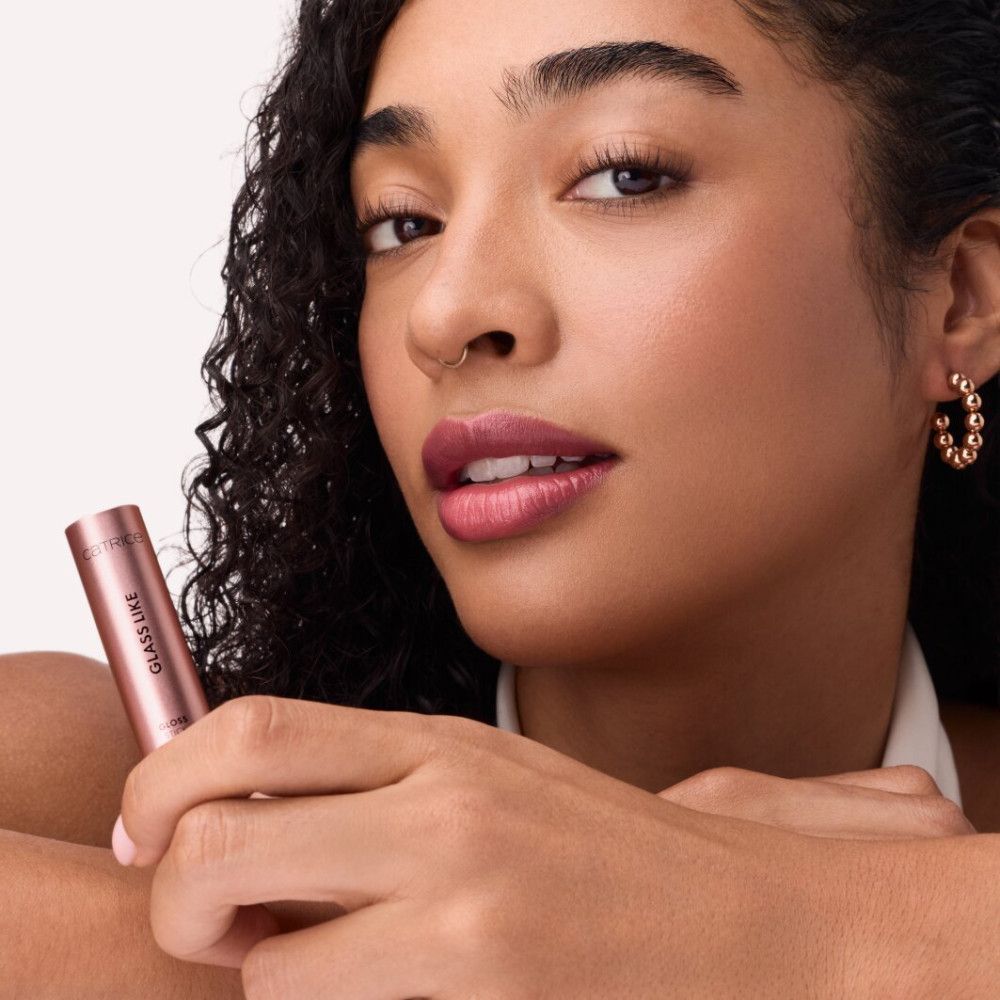 Frau hält einen rosafarbenen Gloss Stick. Aufschrift: GLASS LIKE. Sie trägt rosafarbenen Lippenstift.