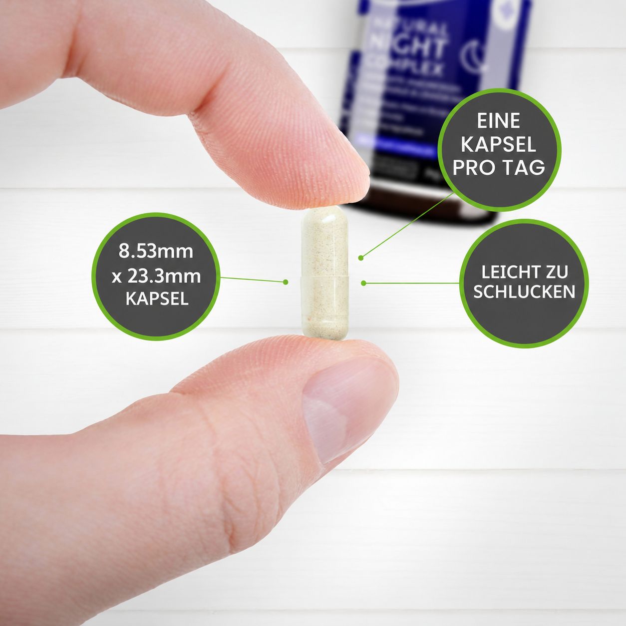 Eine Kapsel mit den Maßen 8,53mm x 23,3mm, gehalten von Fingern. Eine Flasche ist im Hintergrund zu sehen.