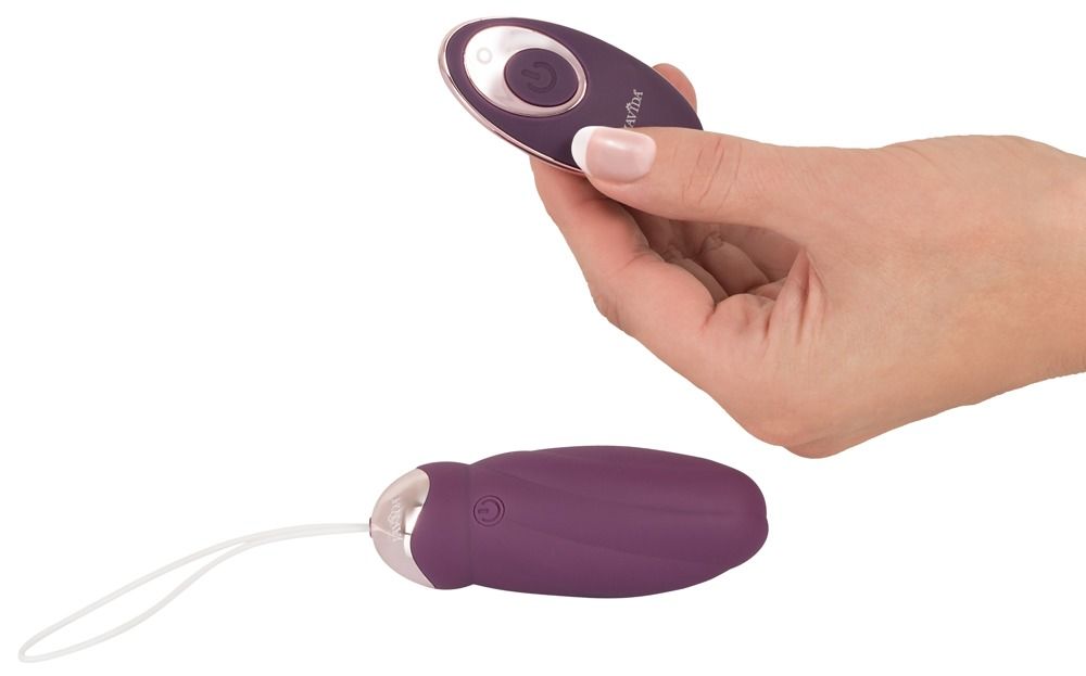 Hand hält Fernbedienung. Lila Vibrator mit weißer Schlaufe. Goldfarbene Akzente. Auf der Fernbedienung ist ein Knopf.