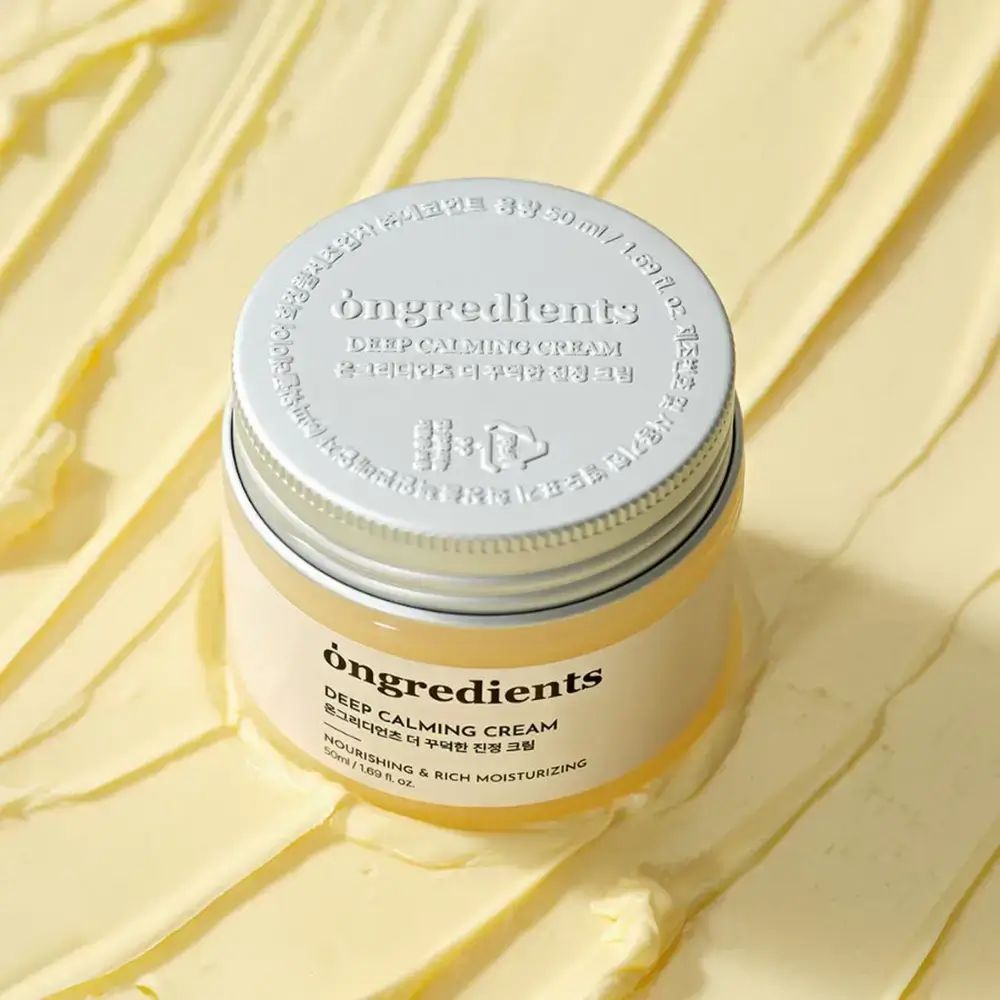 Creme-Tiegel mit silbernem Deckel. Aufschrift: Ongredients, Deep Calming Cream, koreanischer Text, Nourishing & Rich Moisturizing. Creme-Hintergrund.
