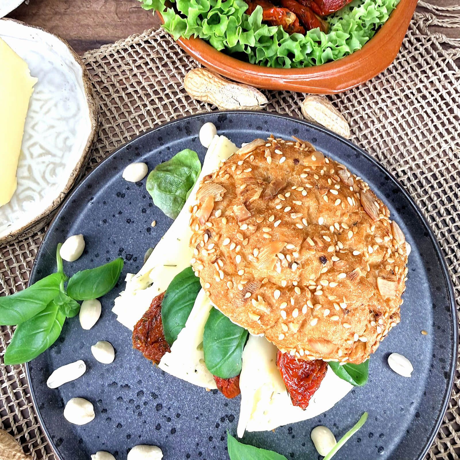 Locawo Erdmännchen Sandwich mit Käse, getrockneten Tomaten und Basilikum auf dunklem Teller.