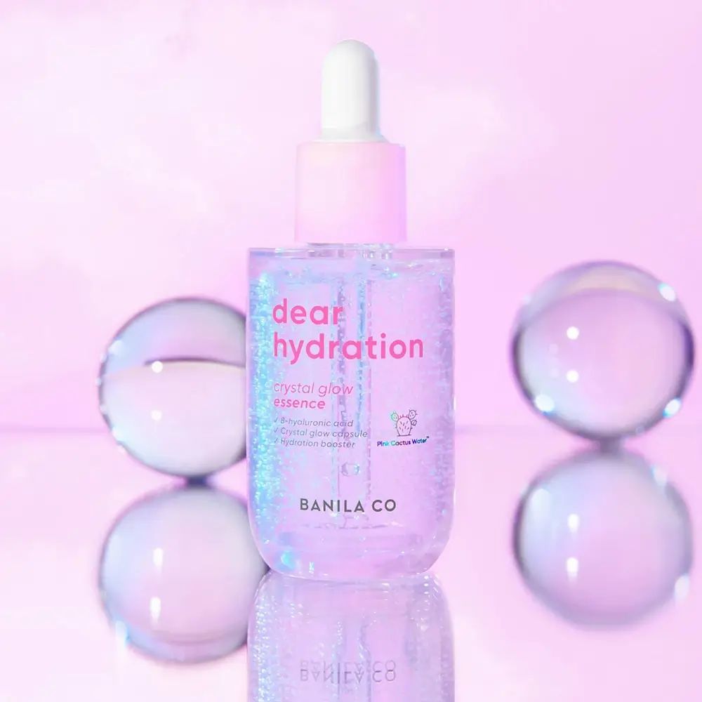 BANILA CO Dear Hydration Crystal Glow Essence. Rosa Flasche mit weißem Deckel und Pipette. Glaskugeln.
