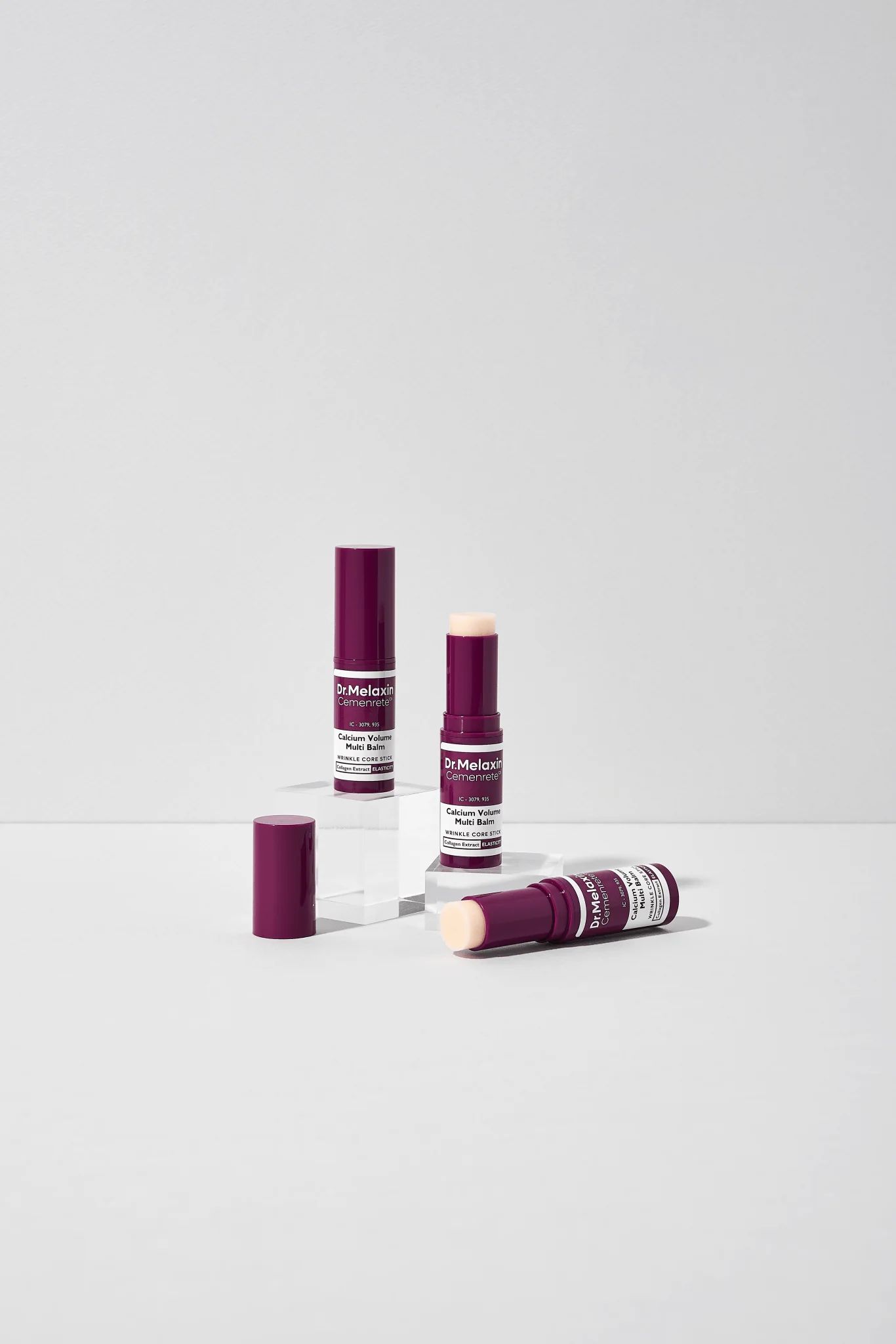 Dr.Melaxin Cemenrete Calcium Volume Multi Balm. Drei Produkte, eines mit geöffneter Kappe. Lila Verpackung.