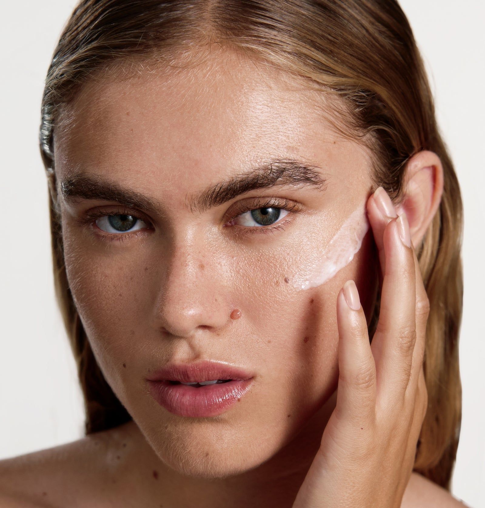 Nahaufnahme eines Gesichts. Eine Hand trägt Serum auf die Haut auf. Sichtbar: Haut und Serum.