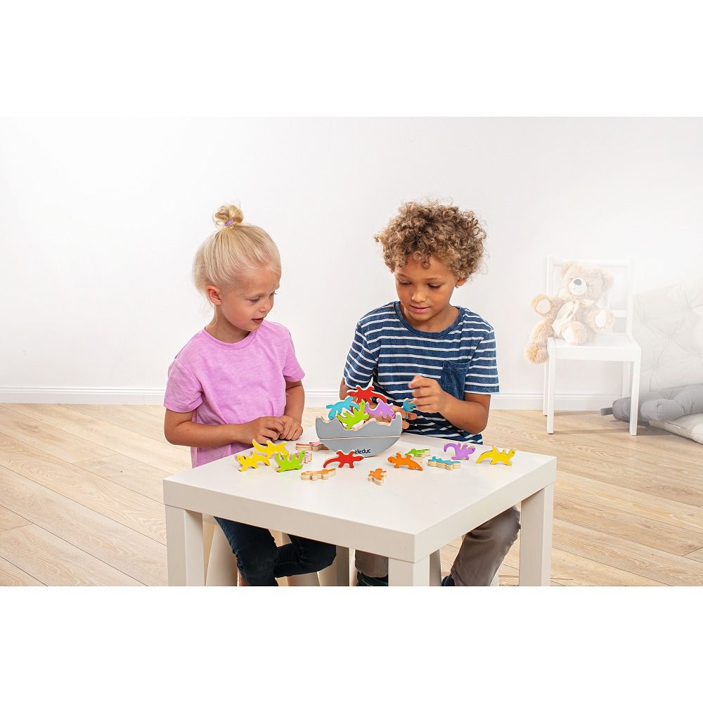 Zwei Kinder spielen mit bunten Holz-Echsen auf einem Tisch. Eine Schüssel mit Echsen.