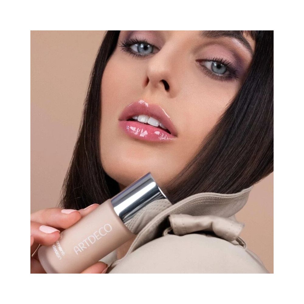 Frau hält Artdeco Rich Treatment Foundation. Flasche mit silbernem Deckel. Marke und Produktname sichtbar.