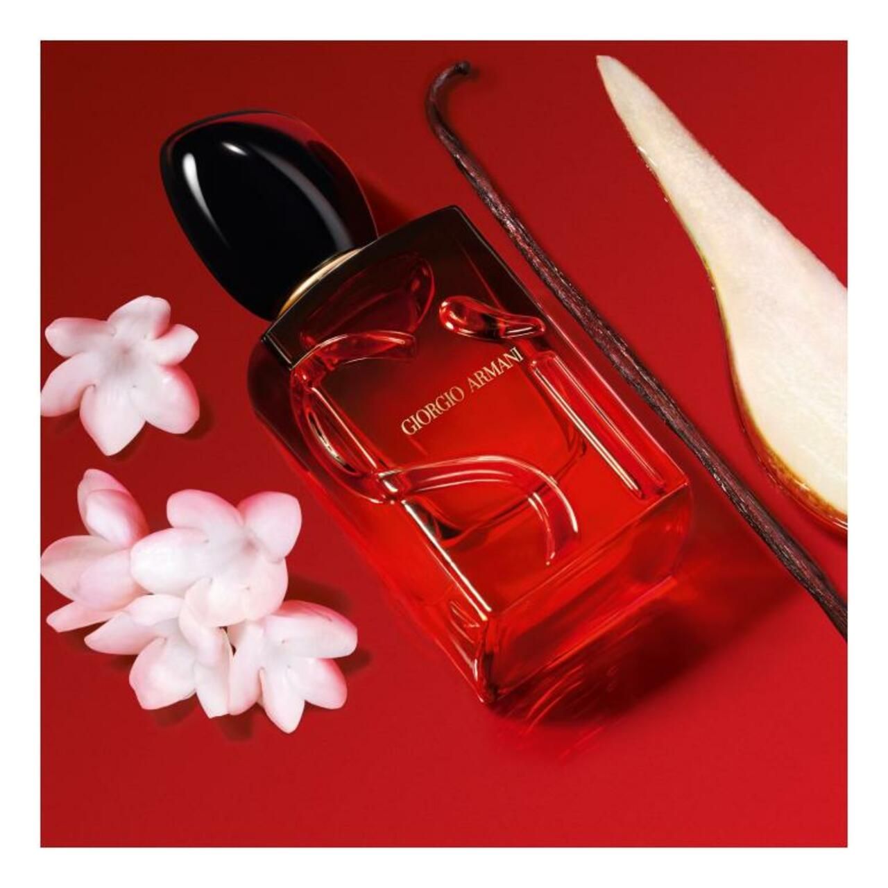 Roter Flakon mit schwarzem Verschluss. Neben Jasminblüten, Vanilleschote und Birne.