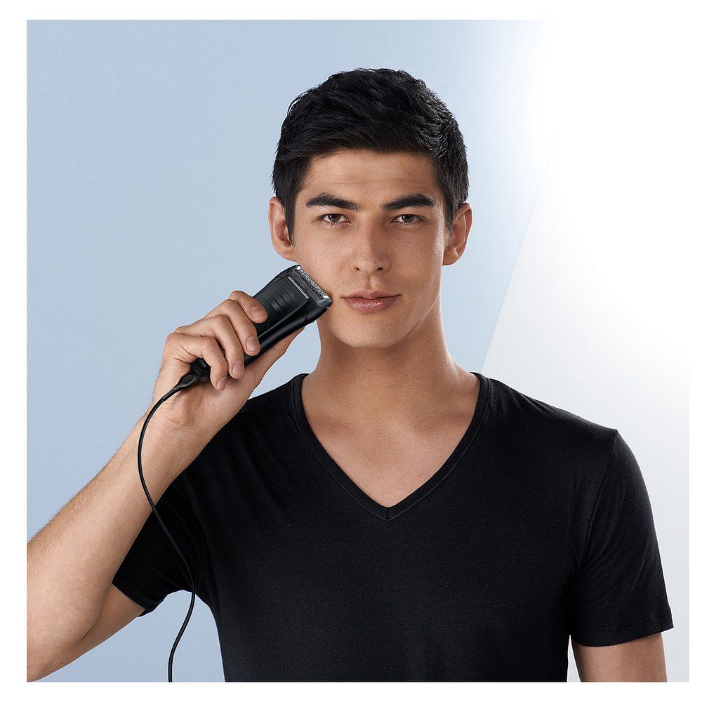 Mann mit Braun Series 1 Elektrorasierer, der sich rasiert. Das Gerät ist mit dem Ladekabel verbunden.