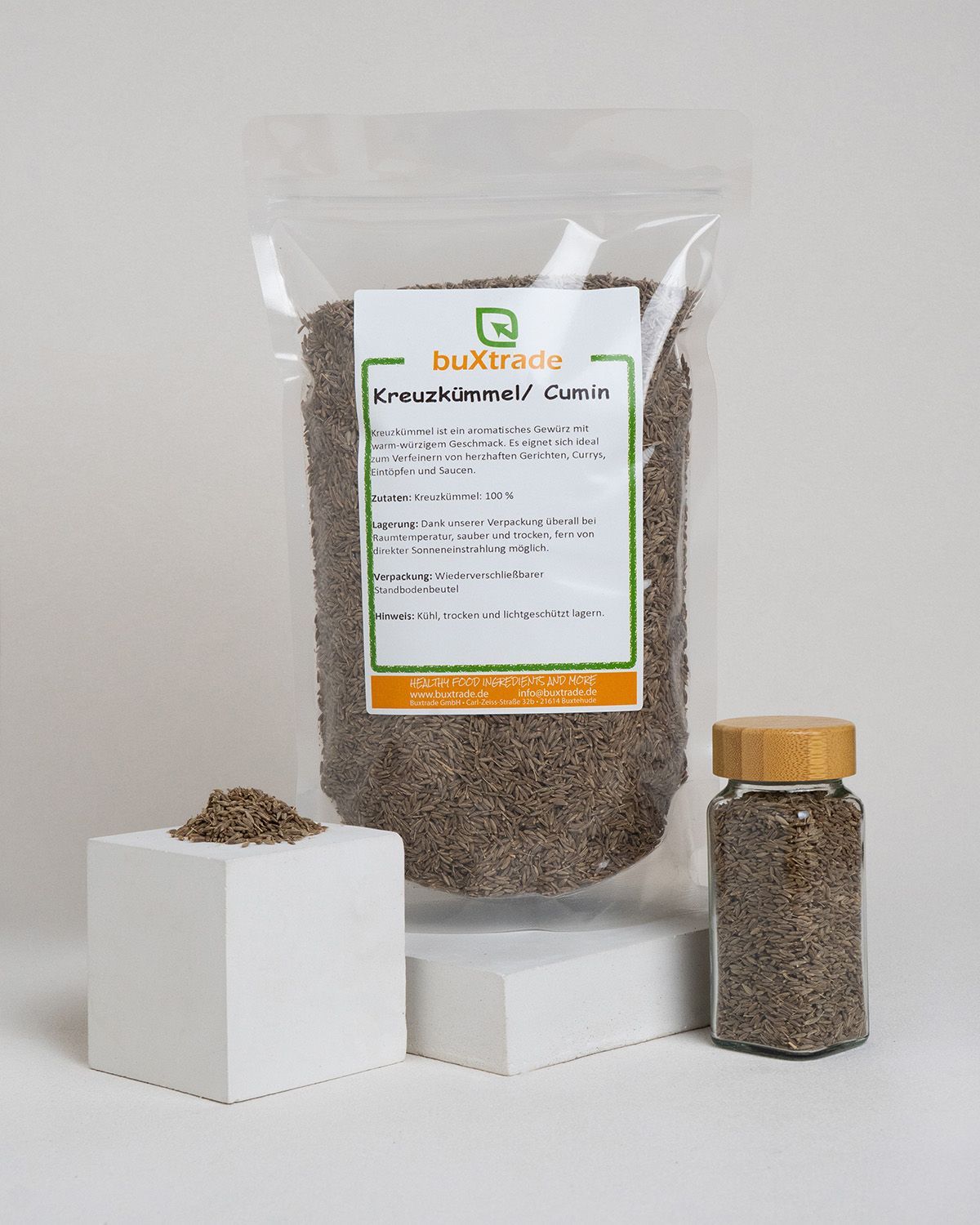 Ein Beutel buxtrade Kreuzkümmel/Cumin, ein kleiner Würfel mit Samen und ein Glas.