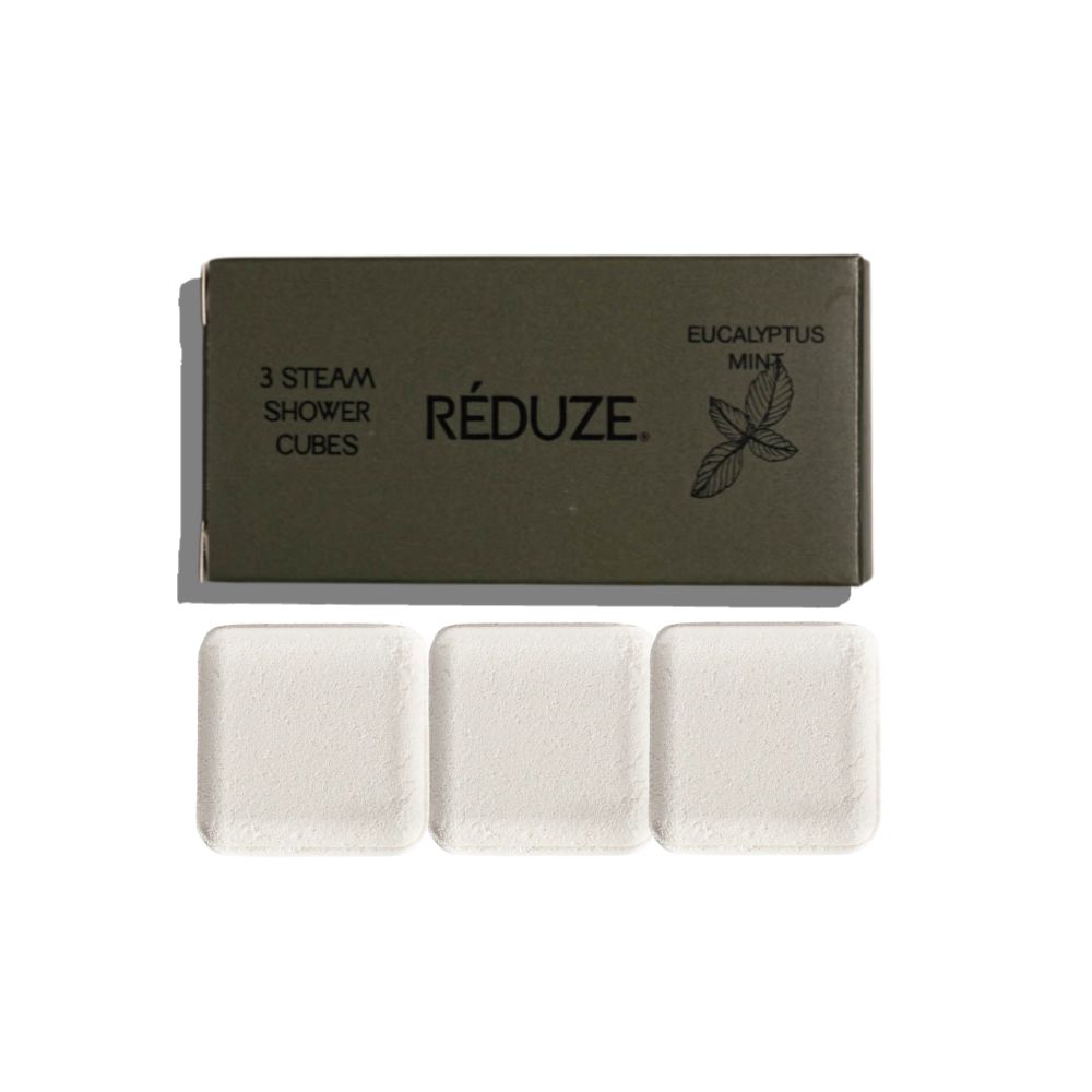 Drei weiße, quadratische Duschwürfel neben einer grünen Schachtel mit Text und Logo.