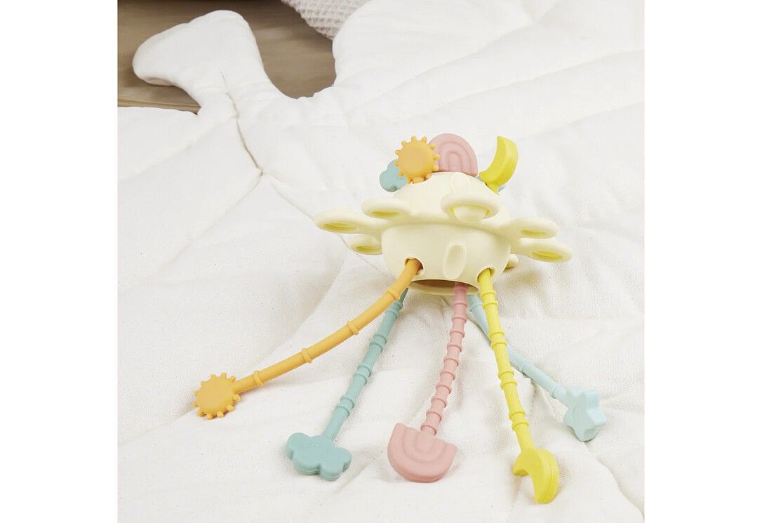 Gelbes Spielzeug mit farbigen Anhängern auf weißer Decke. Anhänger in Form von Stern, Wolke, Schaufel, Sonne und Sichel.