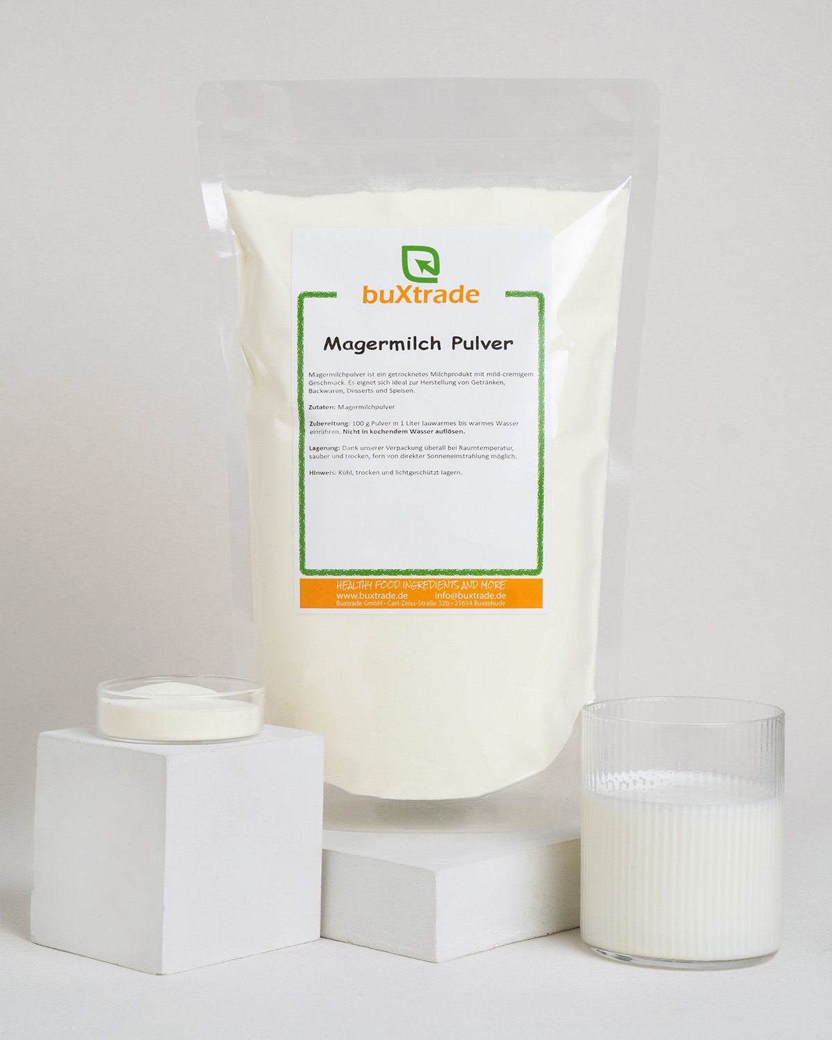 Verpackung mit Magermilchpulver, daneben ein Glas Milch und eine Schale mit Pulver.