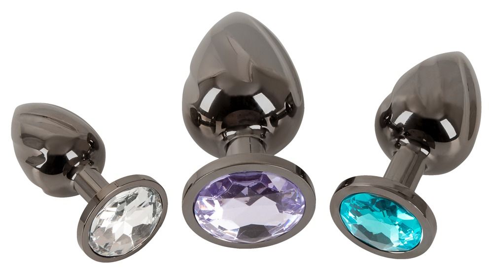 Drei Metall-Analplugs mit Schmucksteinen in Weiß, Türkis und Lila.