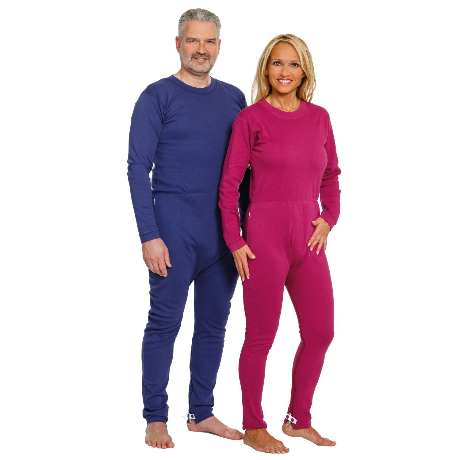 Zwei Personen tragen blaue und pinkfarbene Pflegeoveralls. Langärmlig, mit Reißverschluss am Rücken und Bein. Beide barfuß.