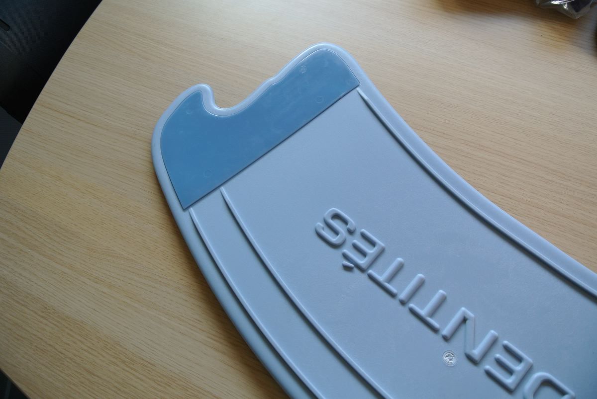 Nahaufnahme eines blauen Transferbretts mit abgerundeter Form und zwei Aussparungen. Aufschrift: IDENTITÉS.