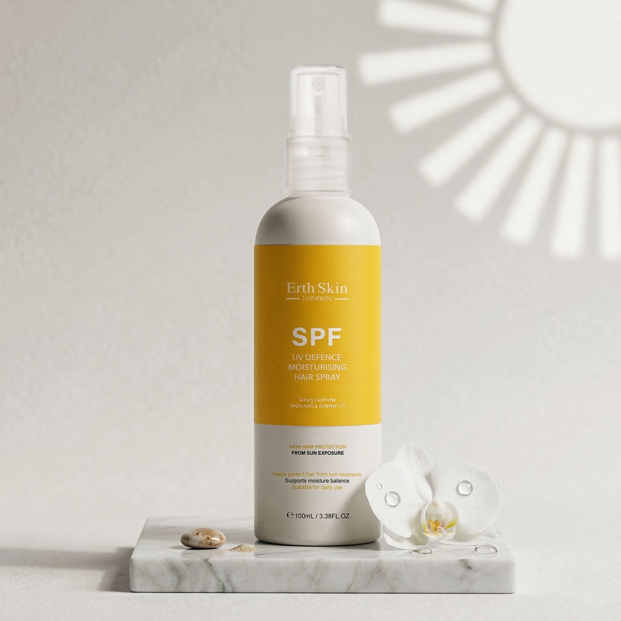 Haarspray-Flasche mit gelbem Etikett. Aufschrift: SPF. ErthSkin London. Auf Marmorplatte mit Blume und Stein.