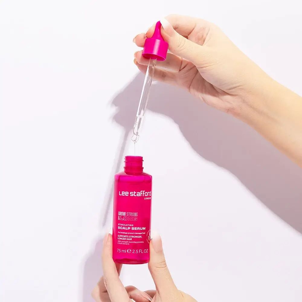 Hände halten eine rosa Pipettenflasche und Pipette des Lee Stafford Grow Strong & Long Serums.