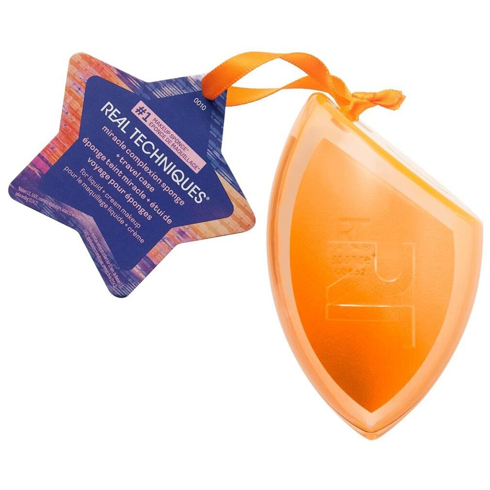 Orangefarbener Make-up-Schwamm in einer transparenten Hülle mit Anhänger. Anhänger mit Text: REAL TECHNIQUES.