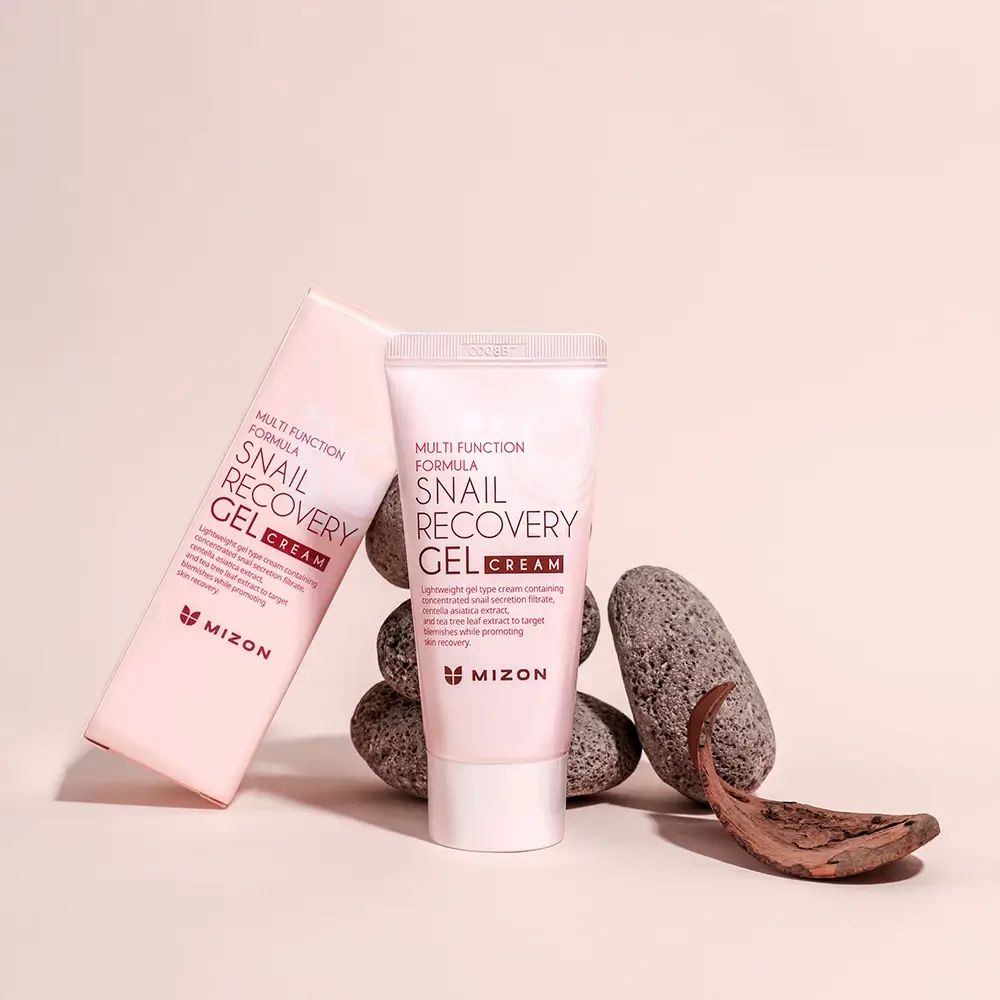 Rosa Tube mit weißem Deckel und Karton. Aufschrift: Snail Recovery Gel Cream. Marke: MIZON. Liegt auf Steinen.