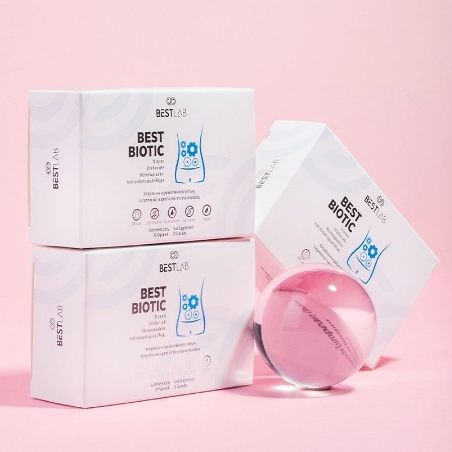 Drei "BEST BIOTIC"-Schachteln, eine mit Kugel. Produktpräsentation auf rosa Hintergrund.
