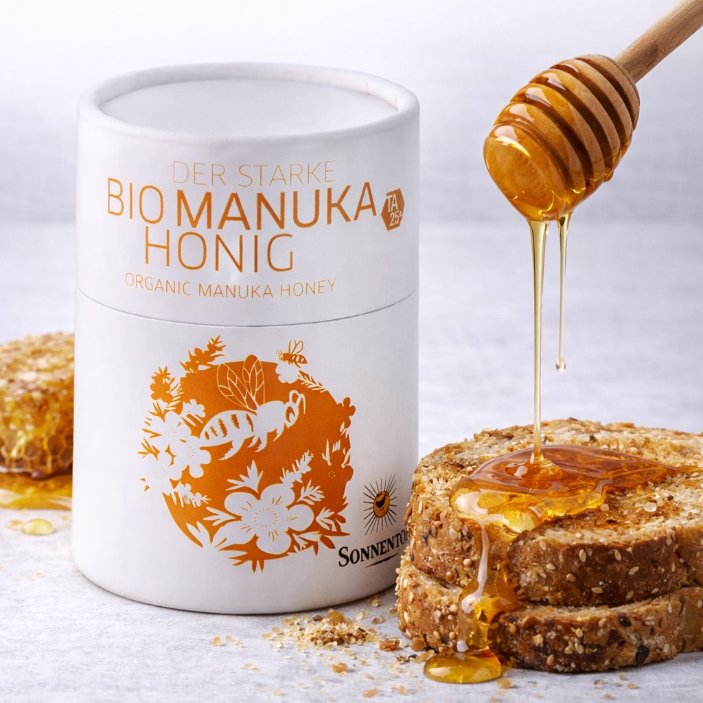 Bio Manuka Honig in weißer Dose mit Bienenmotiv. Honig tropft von einem Holzlöffel auf Brotscheiben.