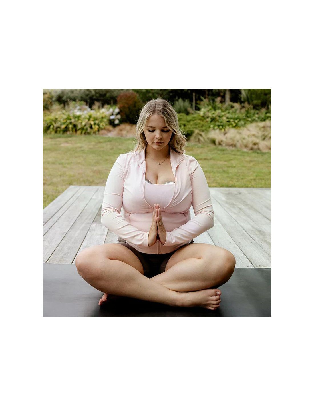 Frau in Meditationshaltung im Freien, trägt Sportkleidung und einen Still-BH.