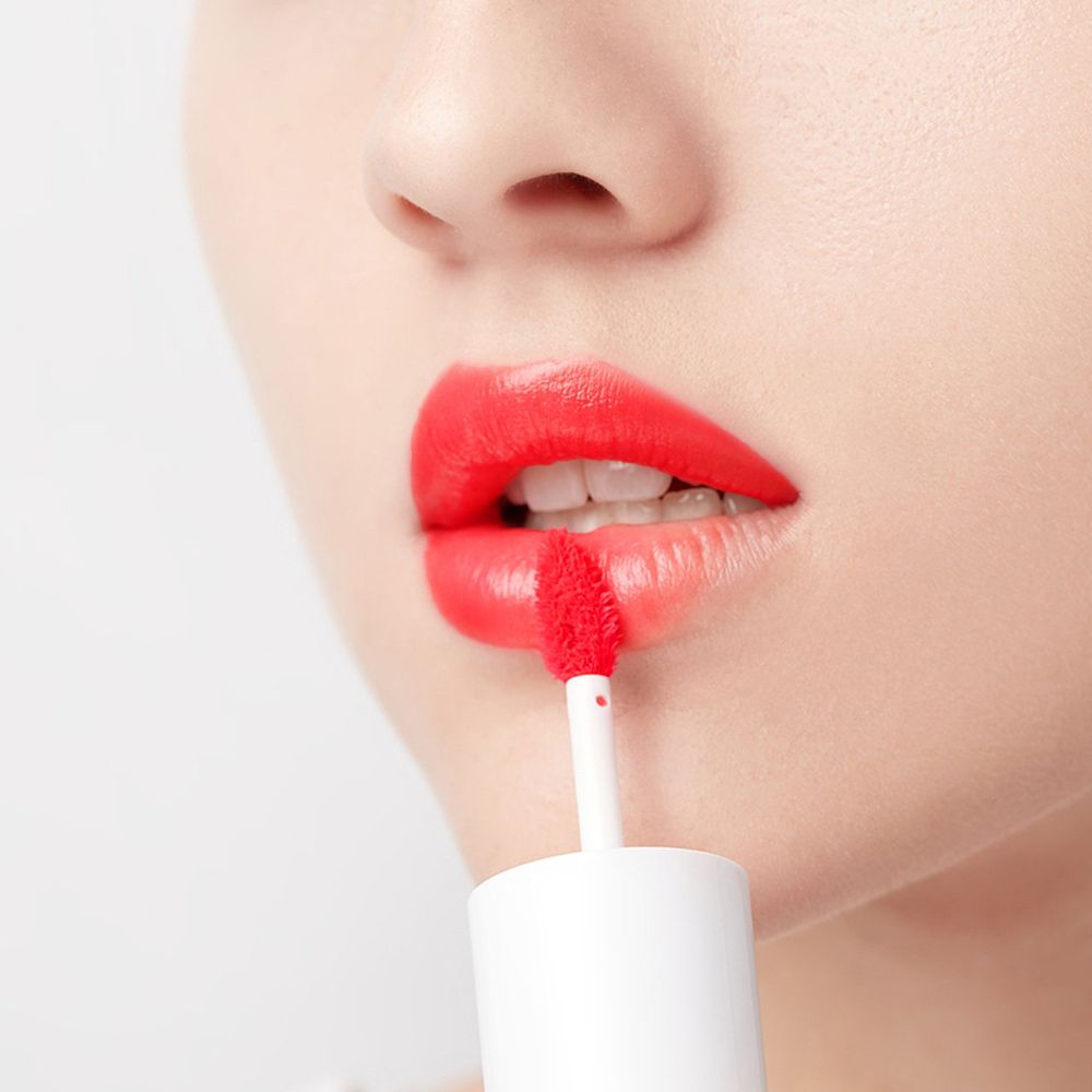 Nahaufnahme von Lippen mit roter Lippenfarbe. Applikator mit roter Farbe. Weiße Kappe. Haut im Hintergrund.