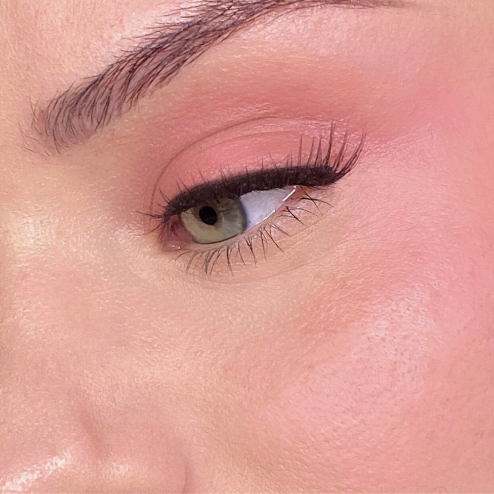 Nahaufnahme eines Gesichts mit rosa Make-up auf Augen und Wangen. Grünes Auge, schwarzer Eyeliner.