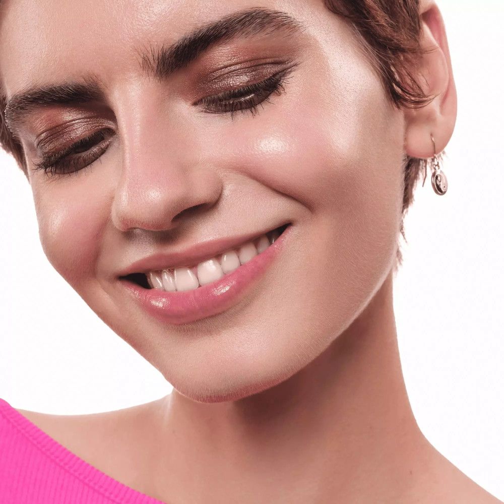 Porträt einer lächelnden Frau mit braunem Lidschatten. Sie trägt ein pinkes Oberteil.